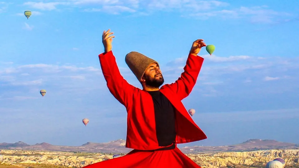 Derviscio rotante in abito rosso che ruota sotto le mongolfiere in Cappadocia